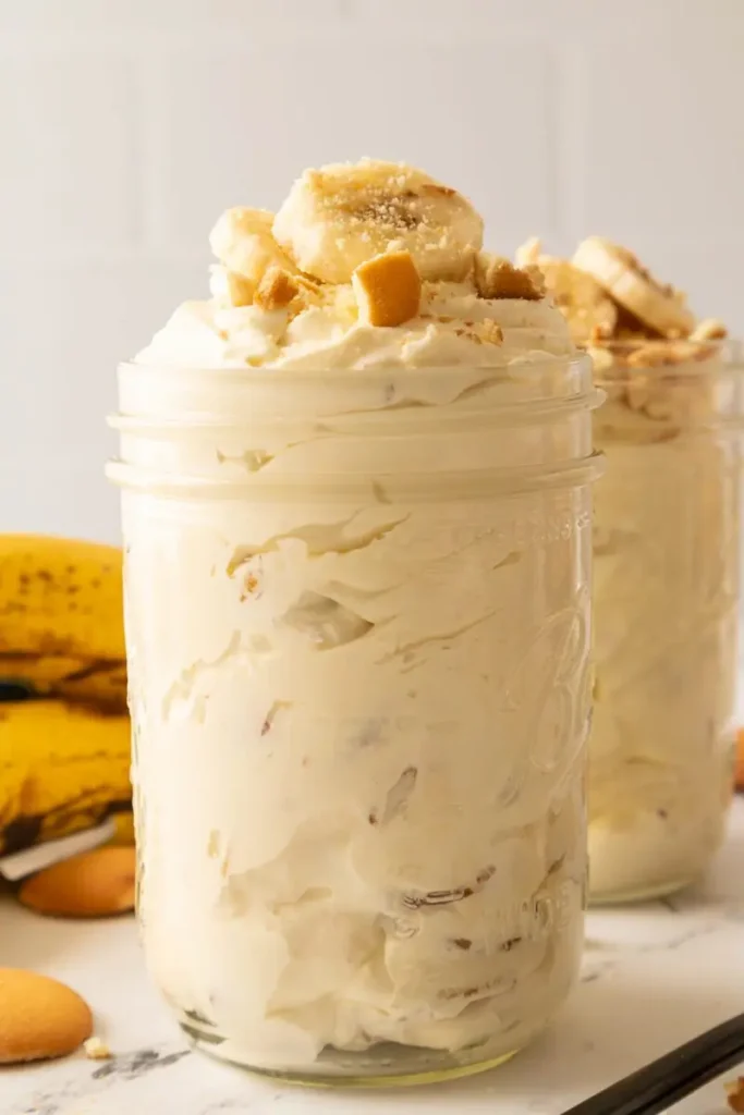 Banana pudding served in a mason jar, topped with banana slices and vanilla wafers.