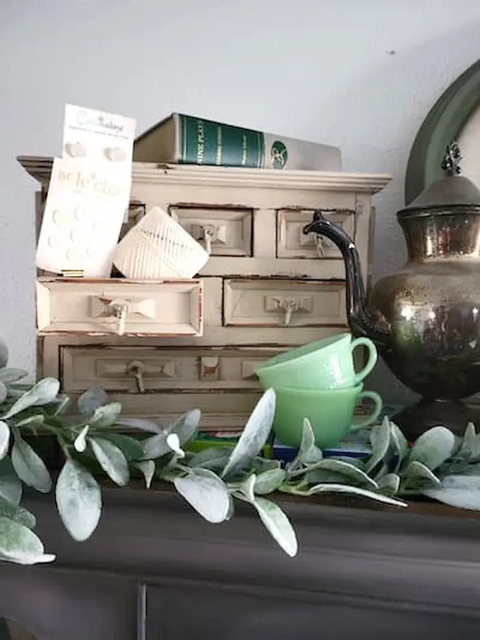 A mantle with a teapot, teacups, and eucalyptus leaves.