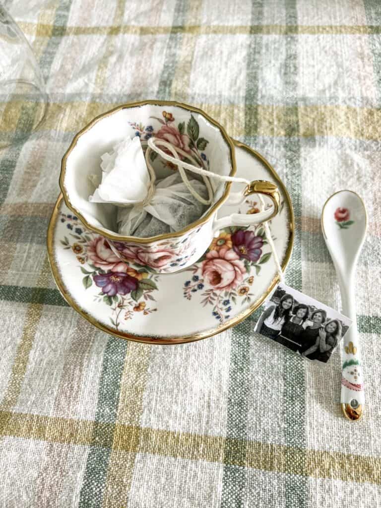 A floral teacup with a teabag and spoon on a checkered tablecloth, along with a photo charm.