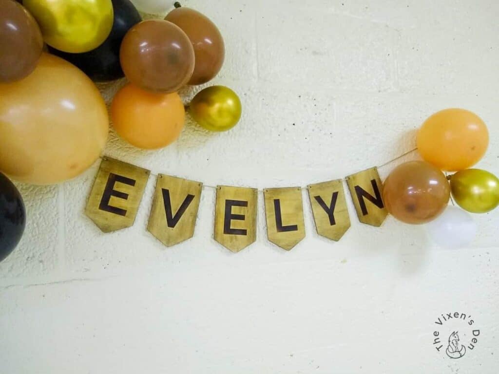Assorted balloons above a banner spelling "evelyn" hung on a textured white wall.