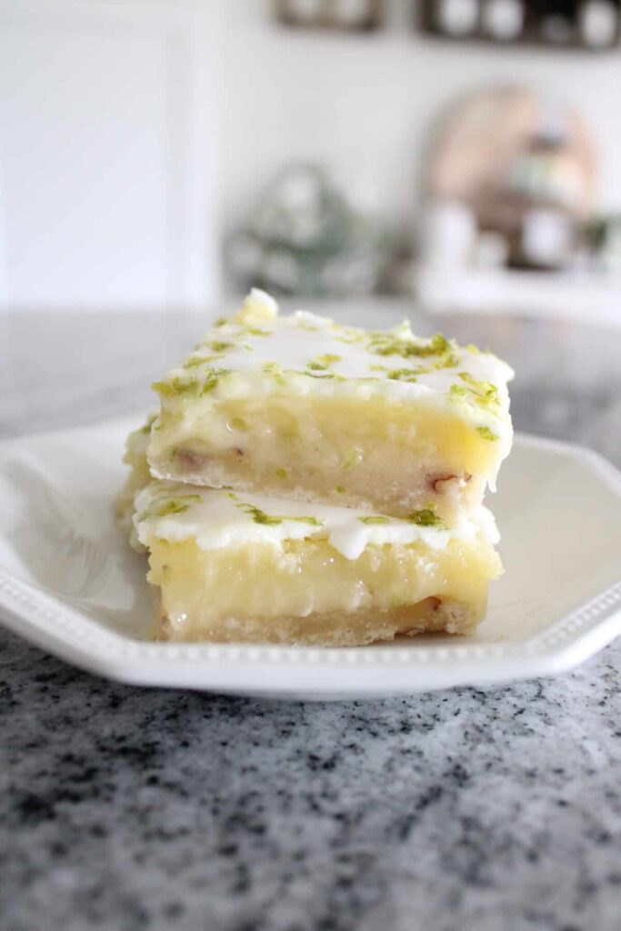 A slice of layered lime bar dessert on a white plate with a kitchen background.
