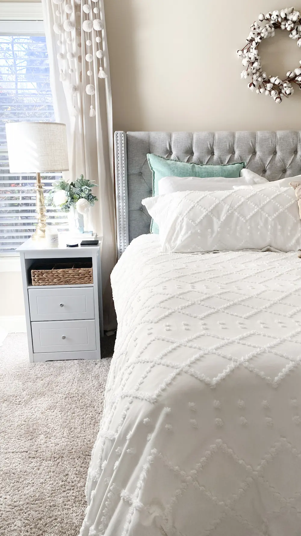 A neatly arranged bedroom with a tufted headboard, white bedding, and a side table with decorative items.