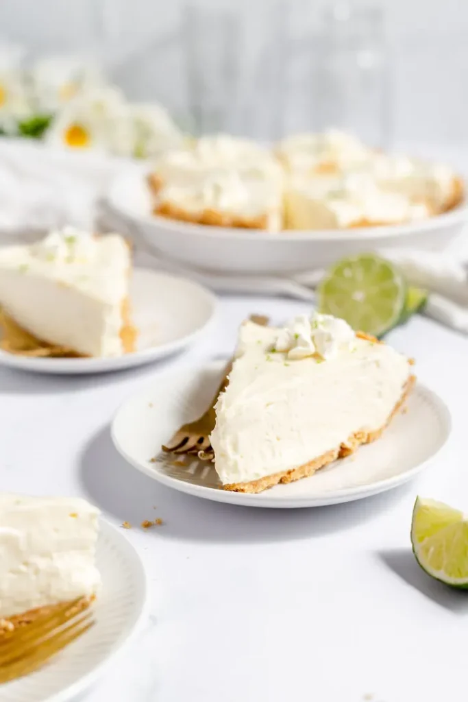 Slices of key lime pie served on individual plates, garnished with lime zest, on a brightly lit table.