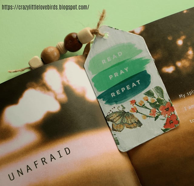 A printed bookmark with the words "read, pray, repeat" resting on an open book with the title "unafraid.