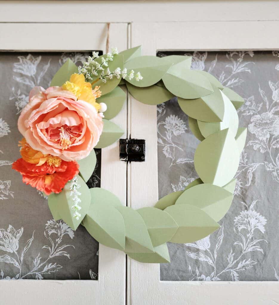 Handmade paper leaf wreath with colorful flowers on a cabinet door.