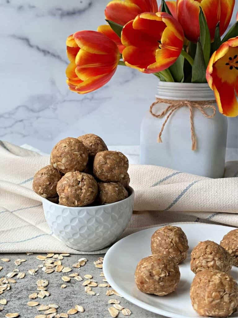 A bowl of oatmeal balls on a plate with a vase of orange tulips in the background.