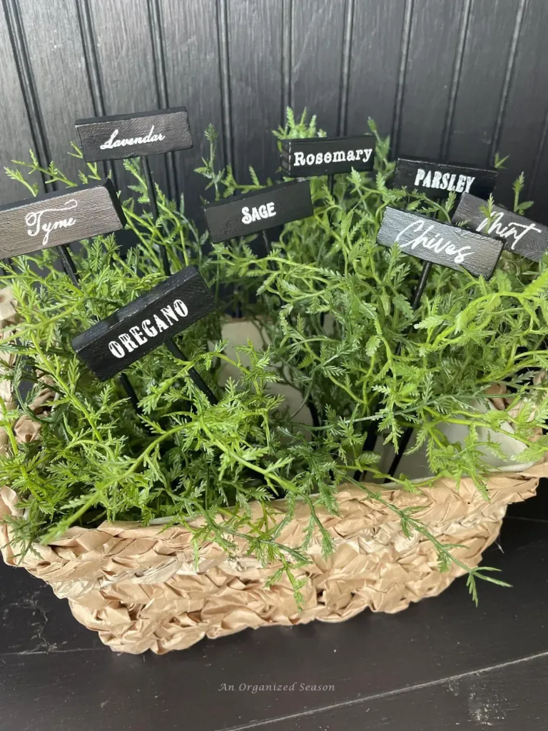 A basket of various herbs including lavender, thyme, rosemary, sage, parsley, oregano, and chive, each labeled with a small black sign.
