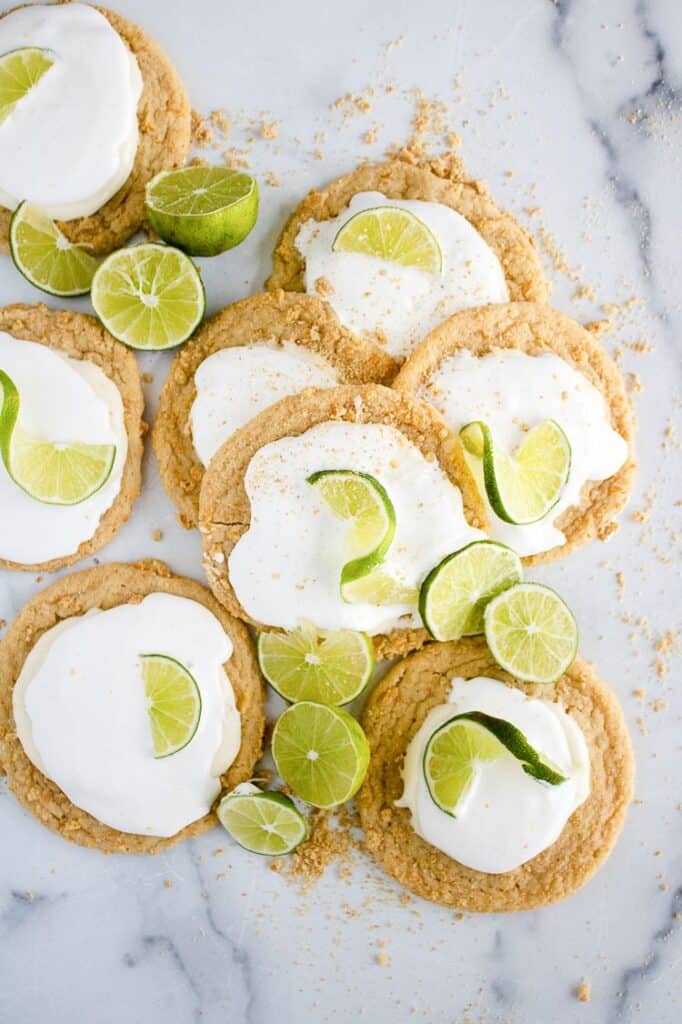 Key lime cookies with white frosting and lime slices on a marble surface.