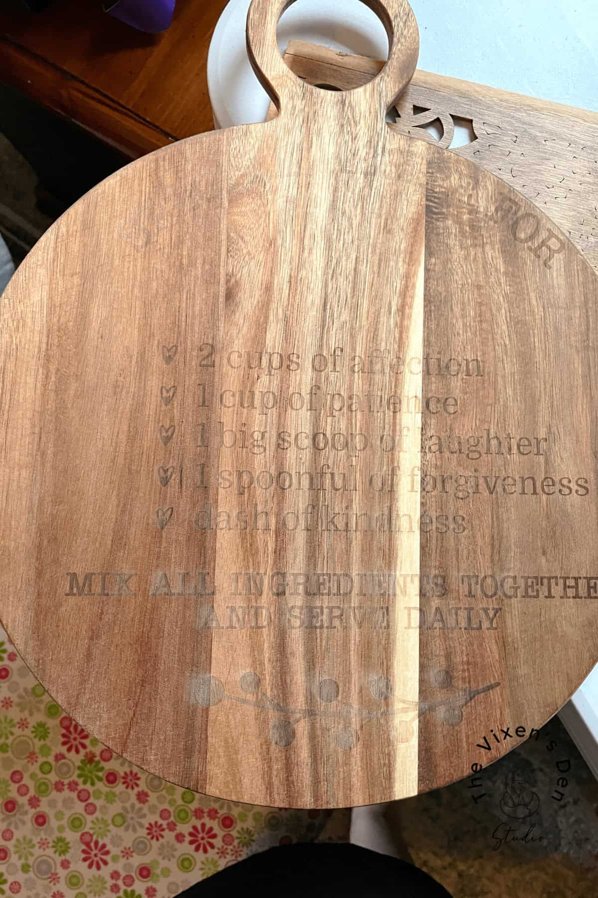 A wooden cutting board with an engraved recipe titled "Recipe for Family." The recipe lists 2 cups of love, 1 cup of patience, 1 big scoop of laughter, 1 spoonful of forgiveness, and a dash of kindness.