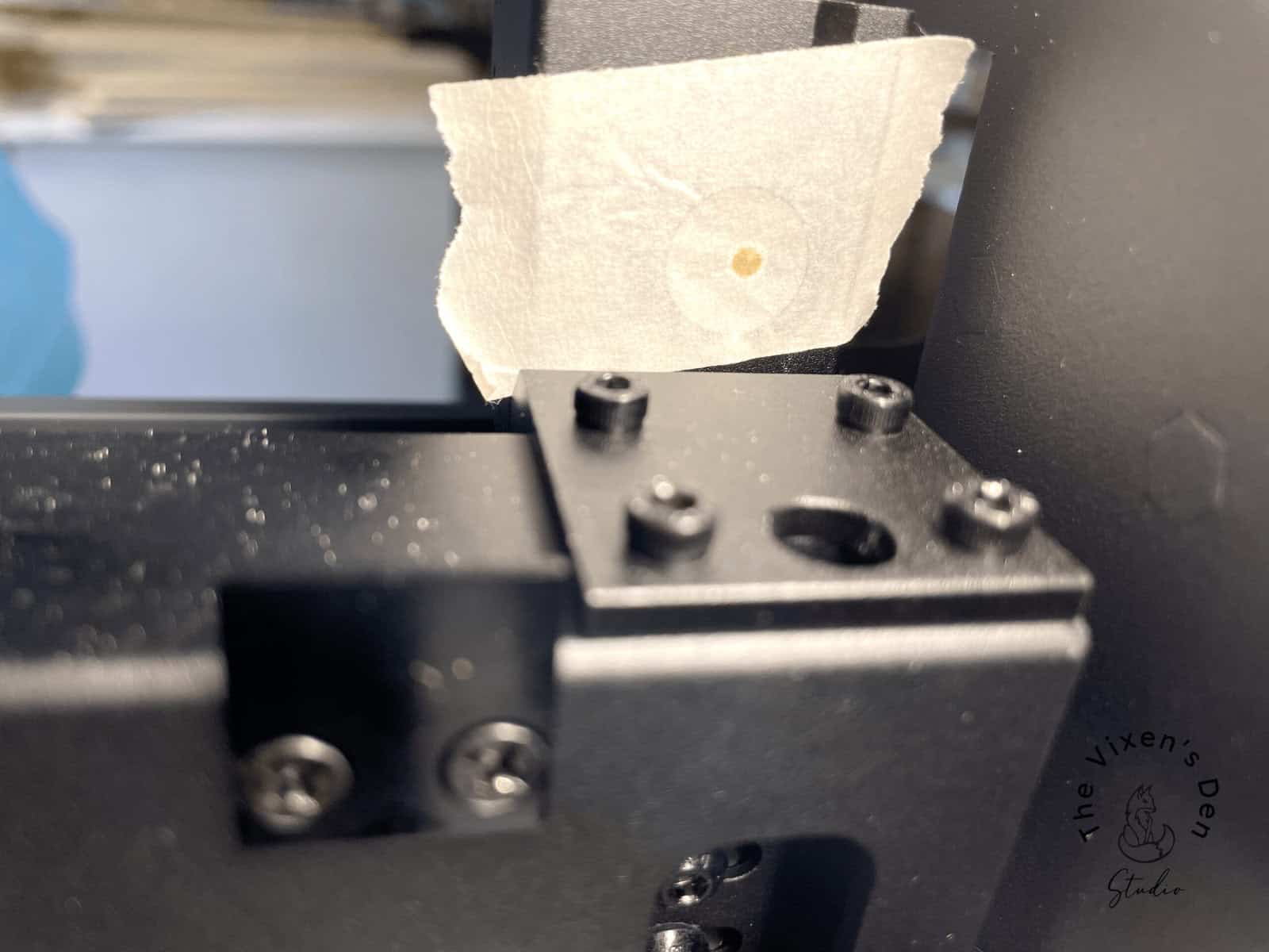 Close-up of a small piece of tape with a tiny hole attached to a black metal object, surrounded by screws.