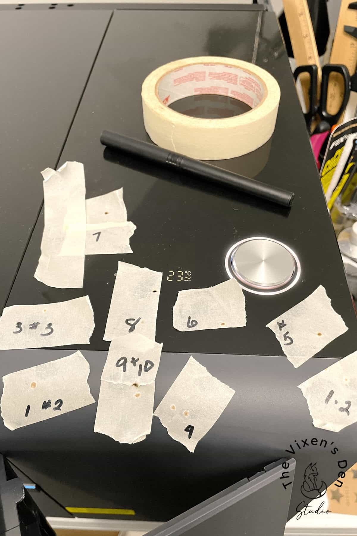 A black table with labeled pieces of masking tape, a roll of tape, a marker, and a pair of scissors on top.