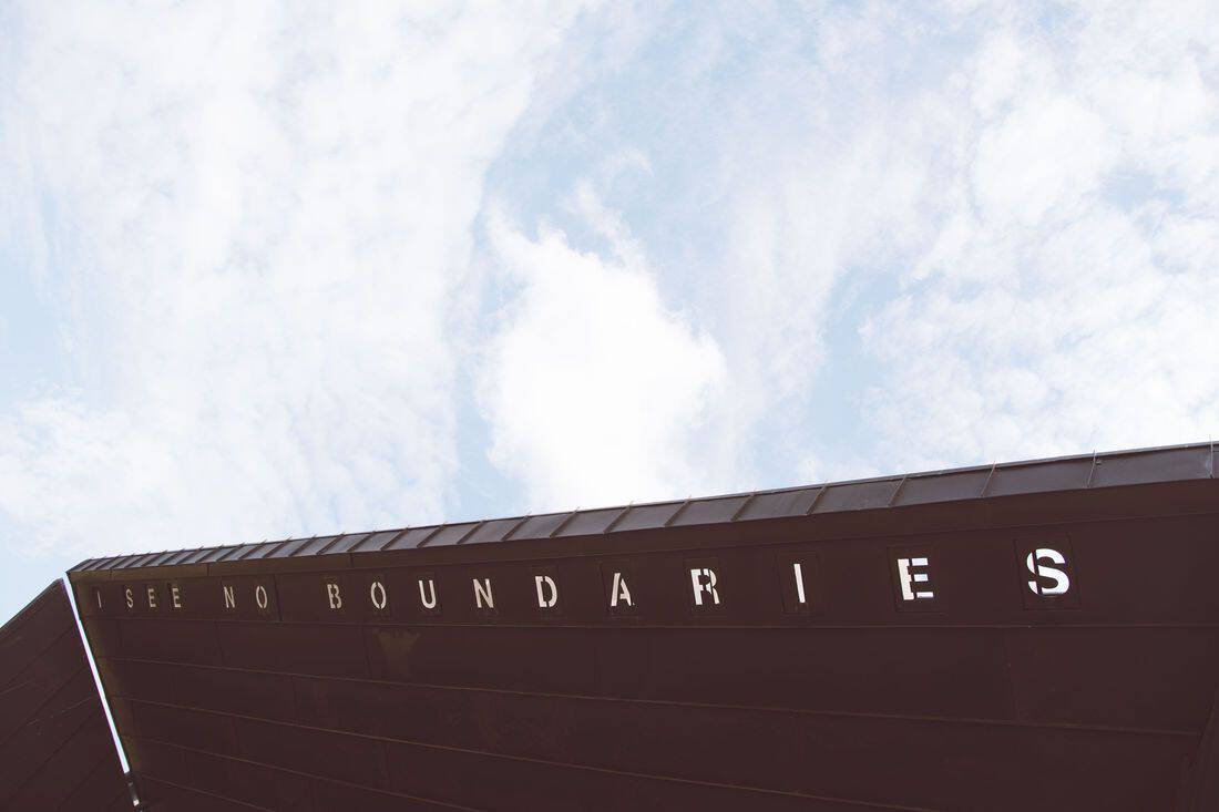 Low-angle view of a building roof edge with the phrase "i see no boundaries" displayed against a cloudy sky.