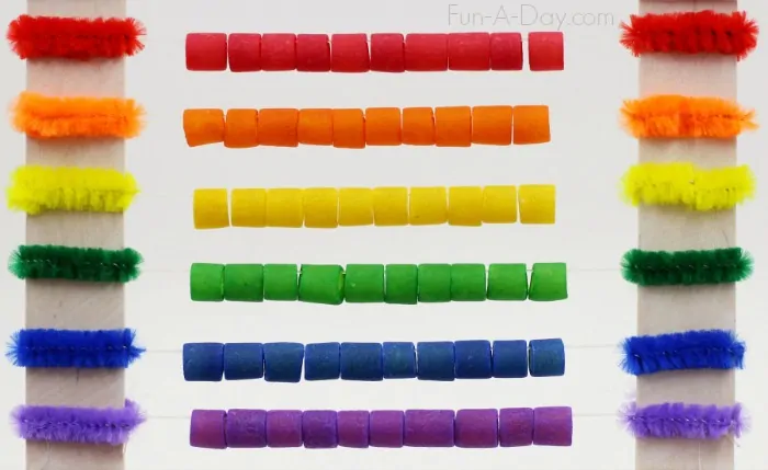 Colorful beads and pipe cleaners organized in horizontal rows by color: red, orange, yellow, green, blue, and purple, attached between two vertical white rods.
