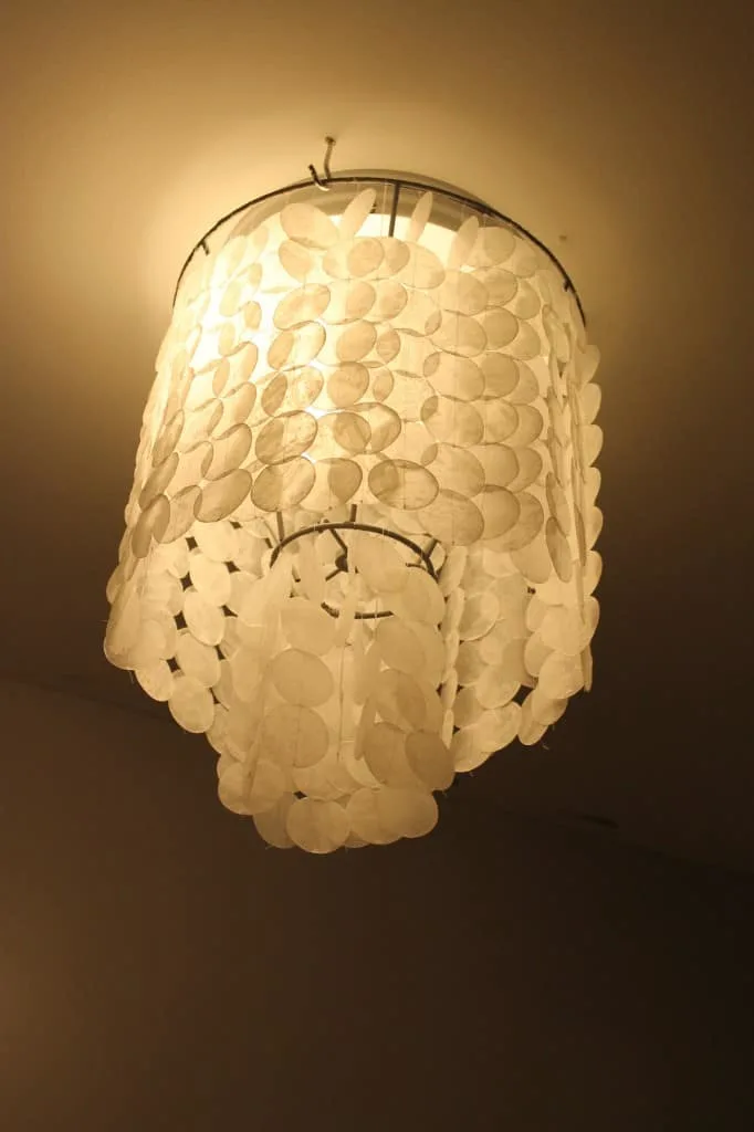 A warm glow from a ceiling light fixture, draped with multiple layers of translucent shell-like discs.