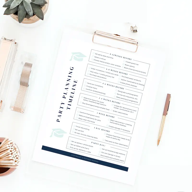 A neatly arranged party planning checklist on a white desk, surrounded by a succulent plant, clipboard, and stationery items.