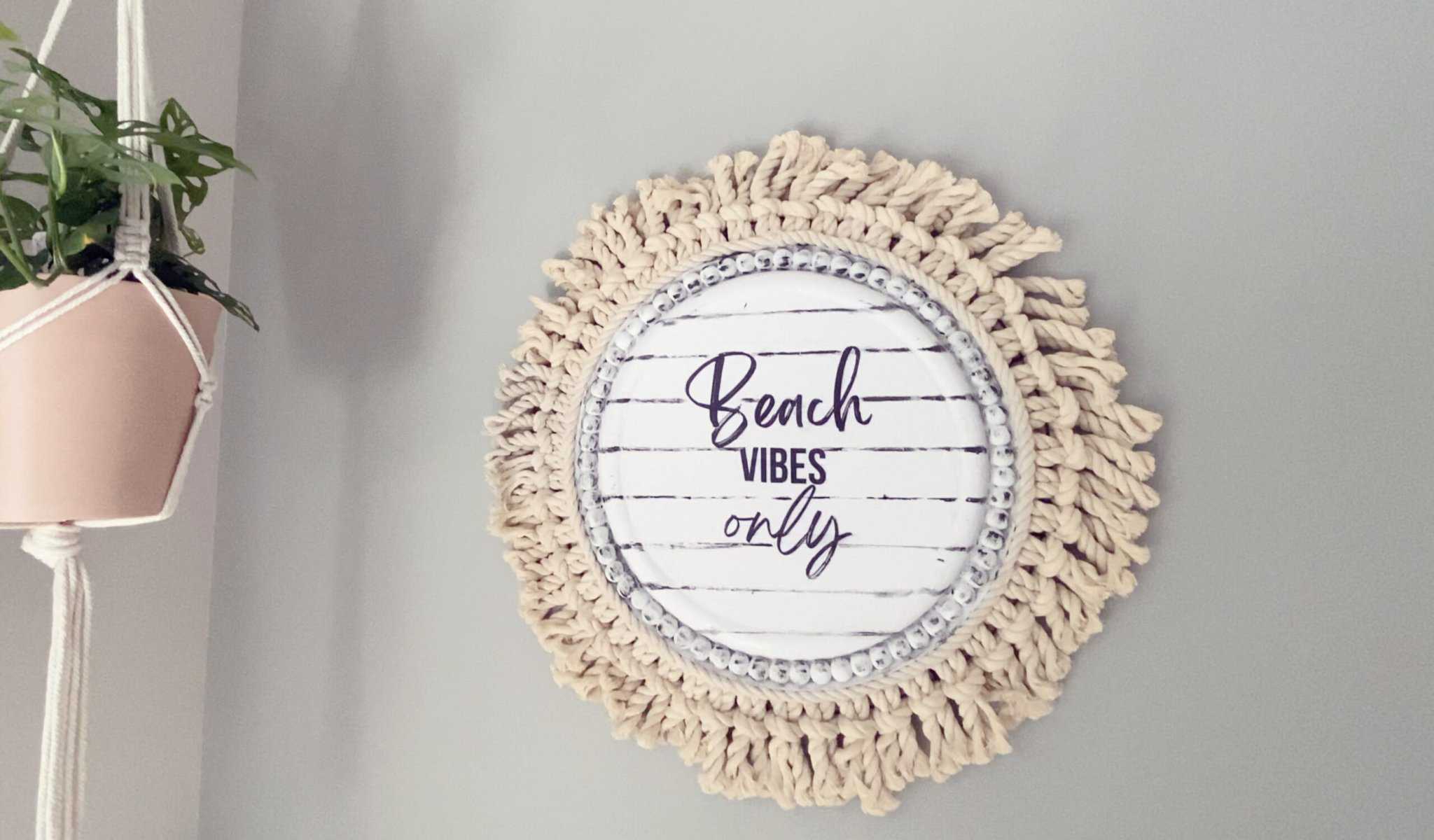 A round, white decorative sign with the text "Beach Vibes Only" hangs on a gray wall next to a hanging plant.