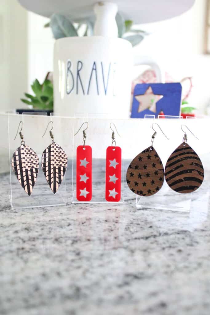 Three pairs of earrings are displayed: one with striped leaves, one with red rectangular pendants and star cutouts, and one with teardrop shapes featuring star and stripe patterns.