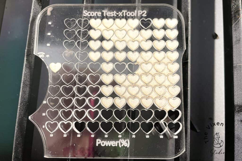 A laser-engraved test sheet displaying an array of heart shapes with varying levels of engraved depth and darkness, marked by power percentages and score test notations.
