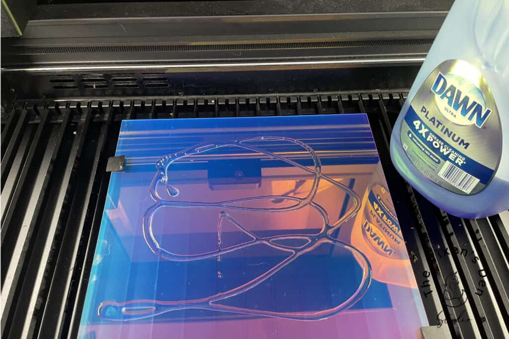 A bottle of Dawn platinum dish soap next to a 3D printer with a partially printed object on a reflective blue and purple printer bed.