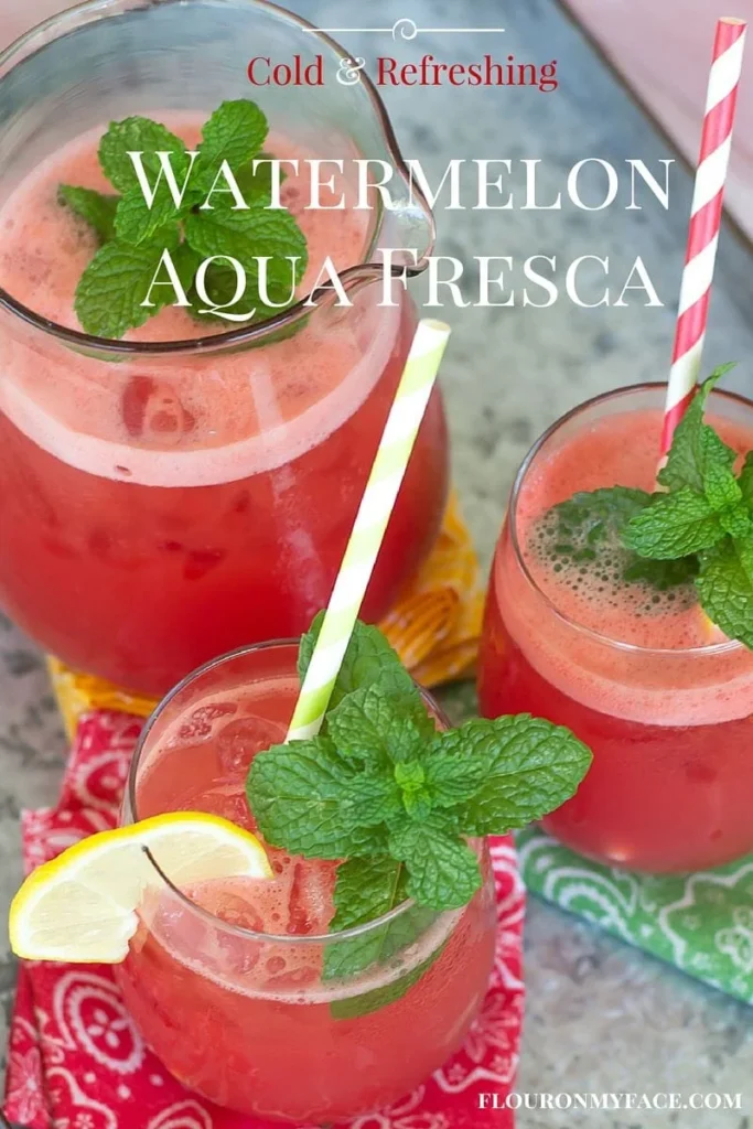 Three glasses of watermelon aqua fresca garnished with mint leaves and lemon slices, with colorful straws and fabric napkins beneath them. The text "Cold & Refreshing Watermelon Aqua Fresca" appears on the image.