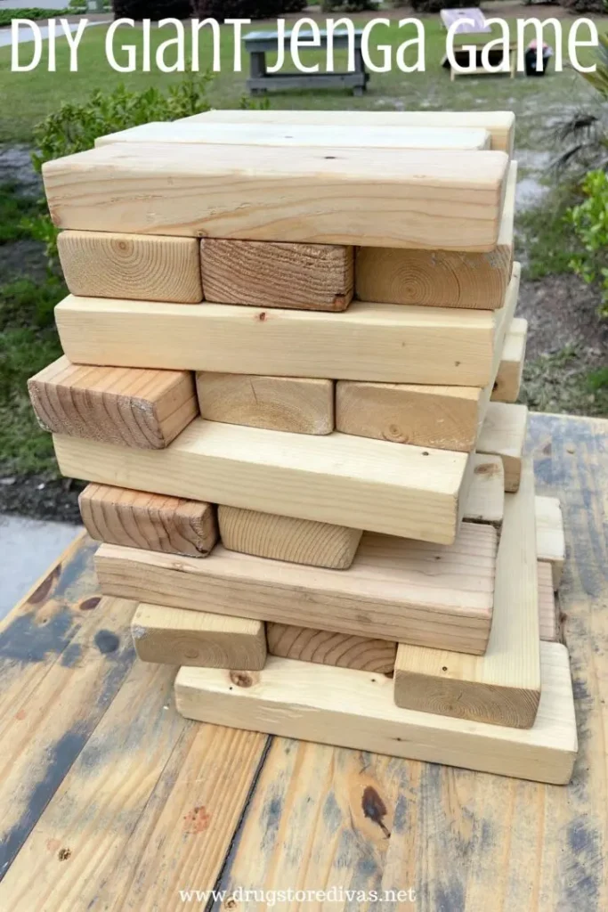 A large Jenga game made from wooden blocks is stacked on a wooden table outdoors. The image has the text "DIY Giant Jenga Game" at the top.