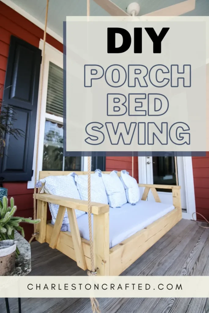 A wooden porch bed swing with light blue cushions is suspended by ropes on a porch. Above the swing is text that reads "DIY Porch Bed Swing." A website link "CharlestonCrafted.com" is at the bottom.