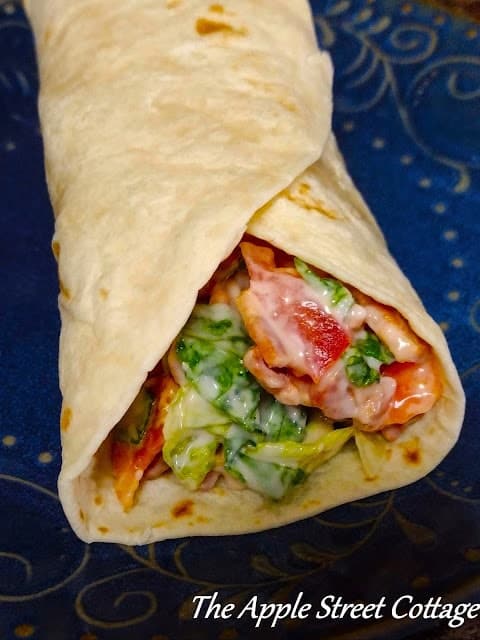 Close-up of a tortilla wrap filled with lettuce, tomatoes, and other ingredients. Text at the bottom reads "The Apple Street Cottage.