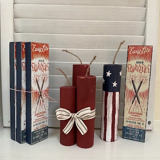 A display of red, white, and blue sparklers and firecrackers, with some tied together with a striped ribbon, next to boxes labeled "EasyLite Gold Sparklers.