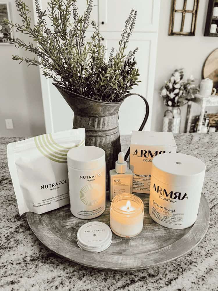 A tabletop display of various wellness and skincare products, including Nutrafol supplements, Arma Colostrum, a small candle, and a potted plant.