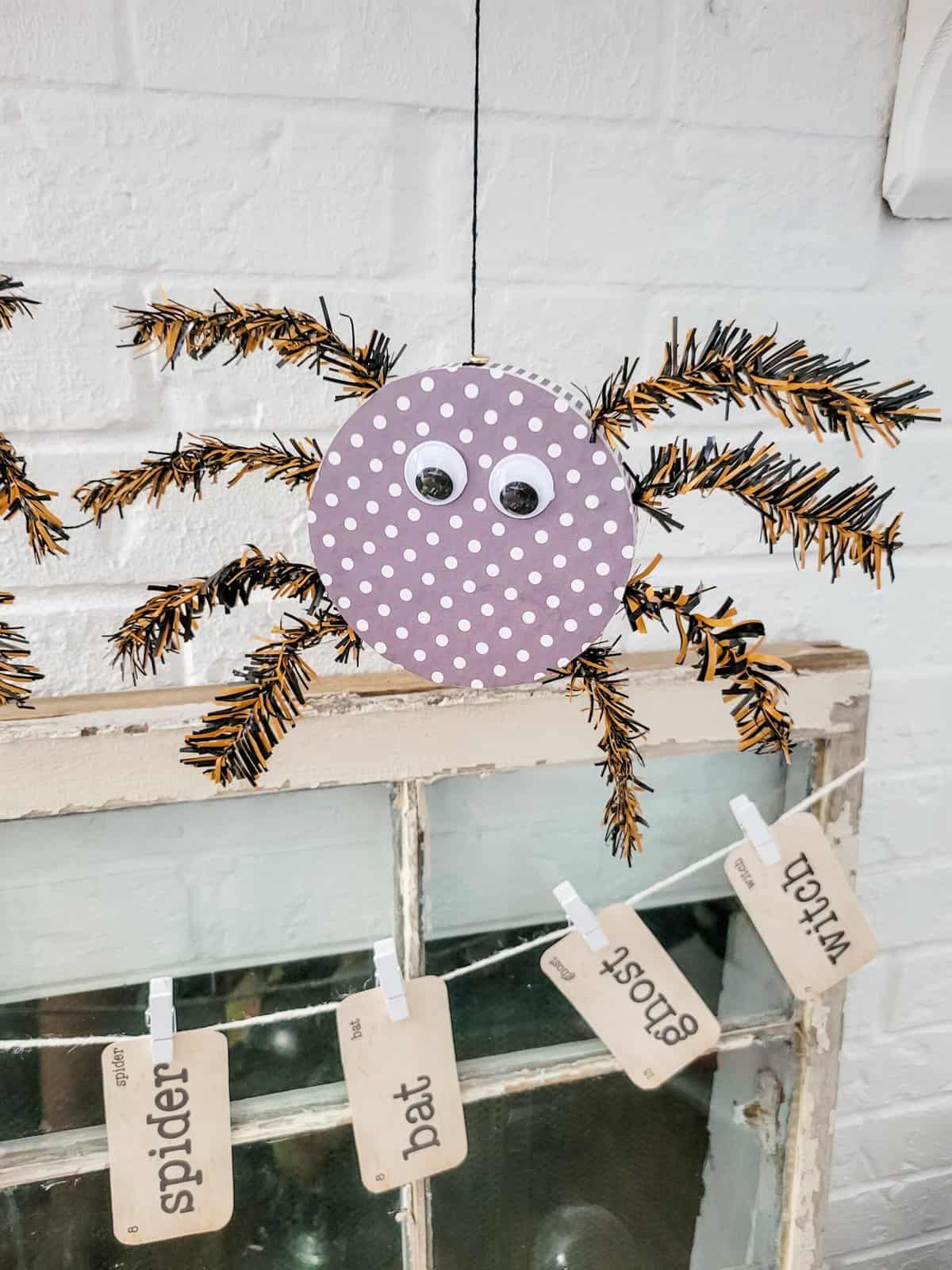 A handmade spider decoration made from a polka-dotted paper circle with googly eyes and pipe cleaner legs. Below it are labels reading, "spider," "bat," "ghost," "witch.