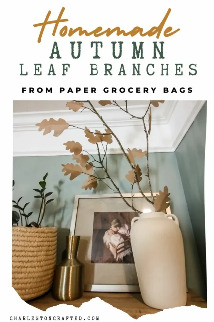 A cream vase with handmade paper leaf branches sits on a shelf decorated with a basket, a gold vase, and a framed picture. Text above reads "Homemade Autumn Leaf Branches from Paper Grocery Bags.