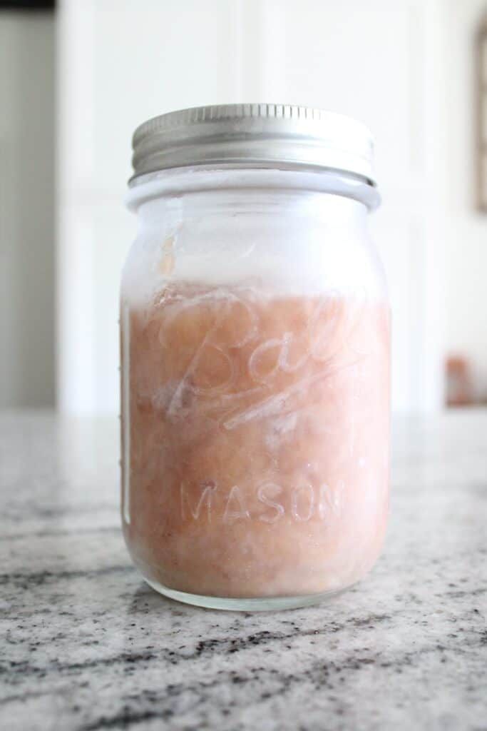 A clear mason jar filled with light pink, slightly frosty contents, placed on a granite countertop.