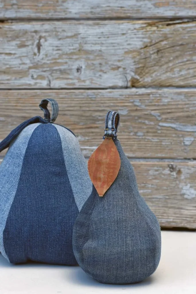 Two fabric pears made from denim with attached fabric stems and leaves set against a weathered wooden background.