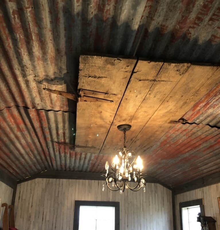 A rustic room with a corrugated metal ceiling, featuring a wooden patch and a hanging chandelier.