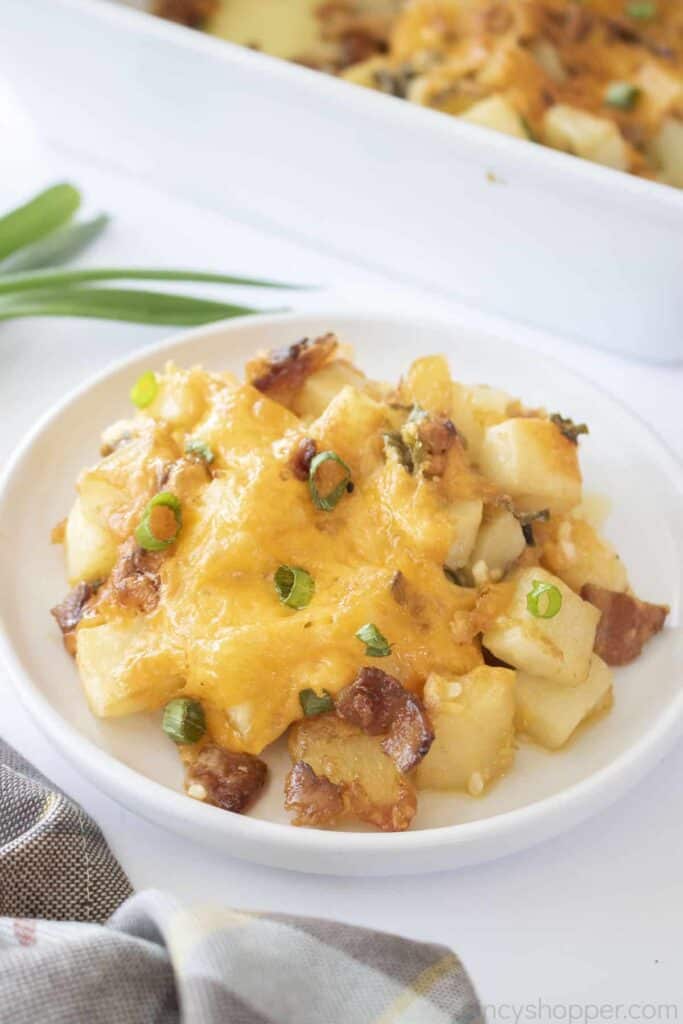 A plate of cheesy potatoes garnished with green onions, next to a checkered cloth.