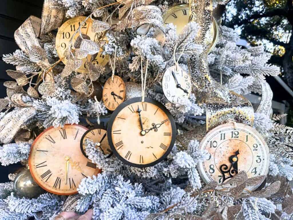 A Christmas tree adorned with small clocks and gold ornaments, surrounded by snowy branches.