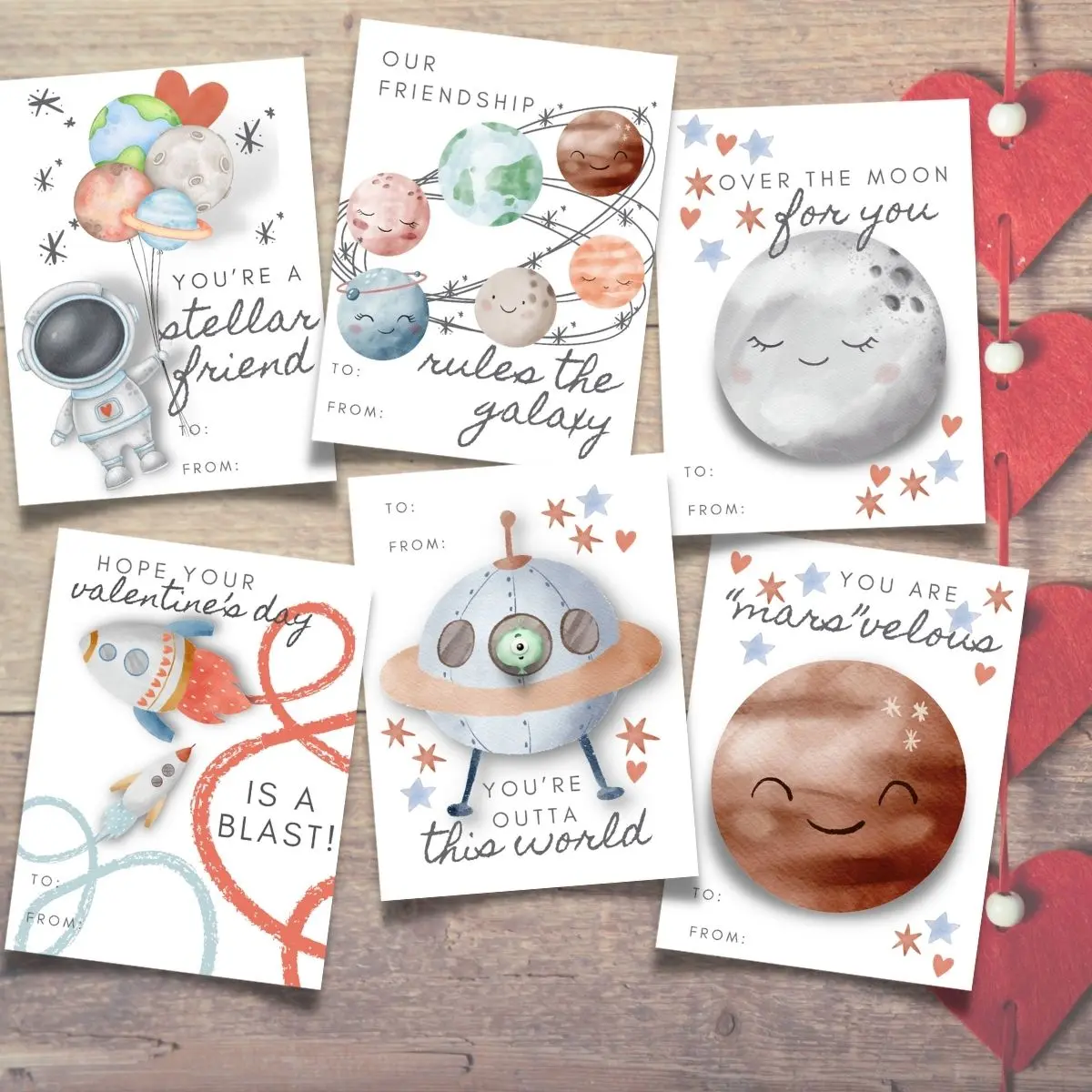 Six illustrated Valentine's Day cards with space-themed designs and puns, placed on a wooden surface with red heart decorations.