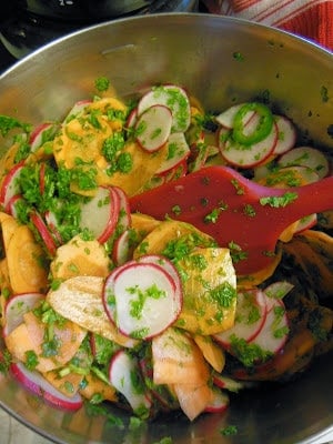 A bowl of salad with sliced radishes, sweet potatoes, parsley, and a red spatula.