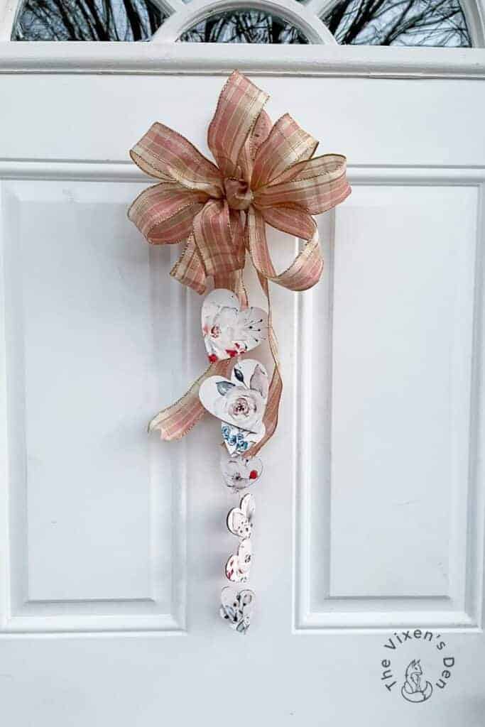 A decorative bow with cascading paper hearts hangs on a white door.