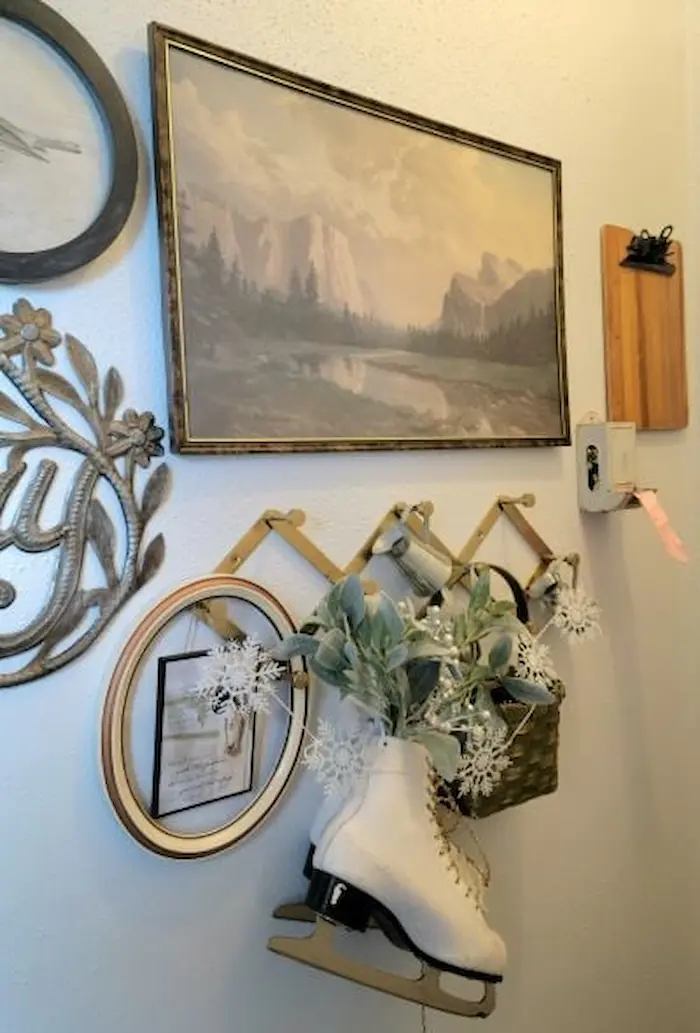 Wall decor includes a painting of mountains, a coat rack with a white ice skate, flowers, framed pictures, and a clipboard with paper.