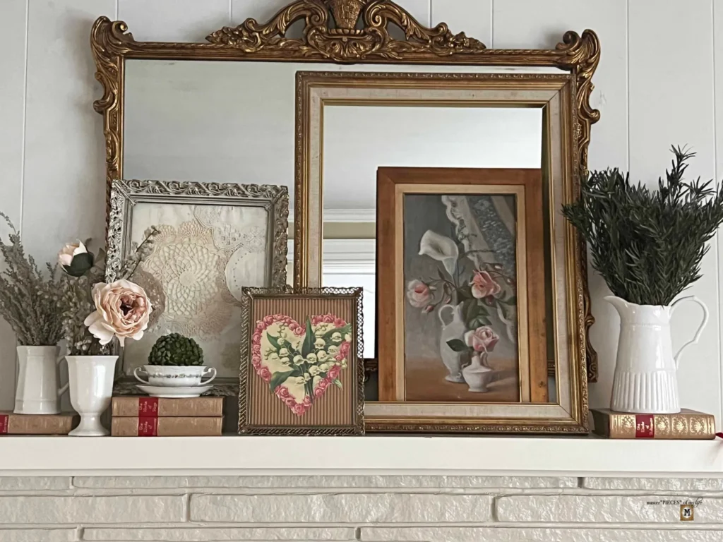 Mantel with ornate mirrors, framed art, flowers, and vintage books.