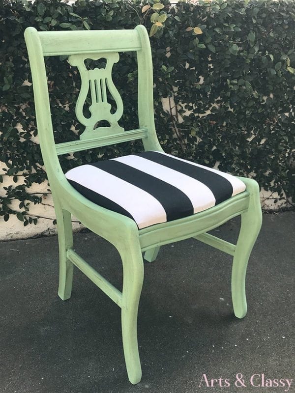 Mint green wooden chair with a lyre-shaped backrest and black-and-white striped cushion, placed outdoors on pavement.