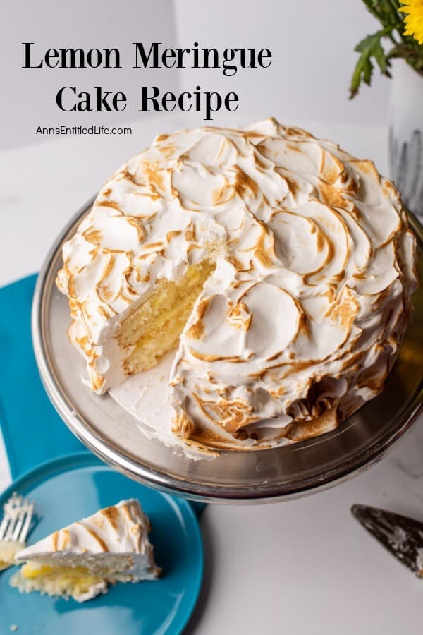 Lemon meringue cake on a stand with a slice removed, showing the layers. A slice on a blue plate with a fork is in the foreground.