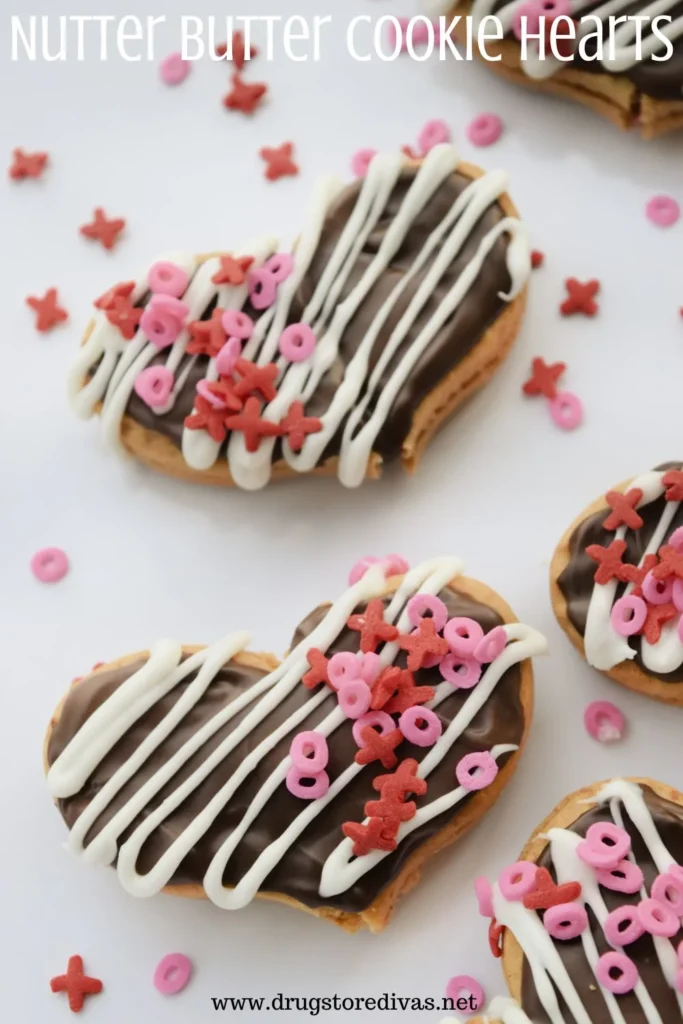 Heart-shaped cookies with chocolate coating, white icing drizzle, and pink-red sprinkles arranged on a white background.