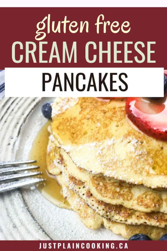 A stack of gluten free cream cheese pancakes topped with strawberry and syrup, served on a plate with a fork and blueberries.