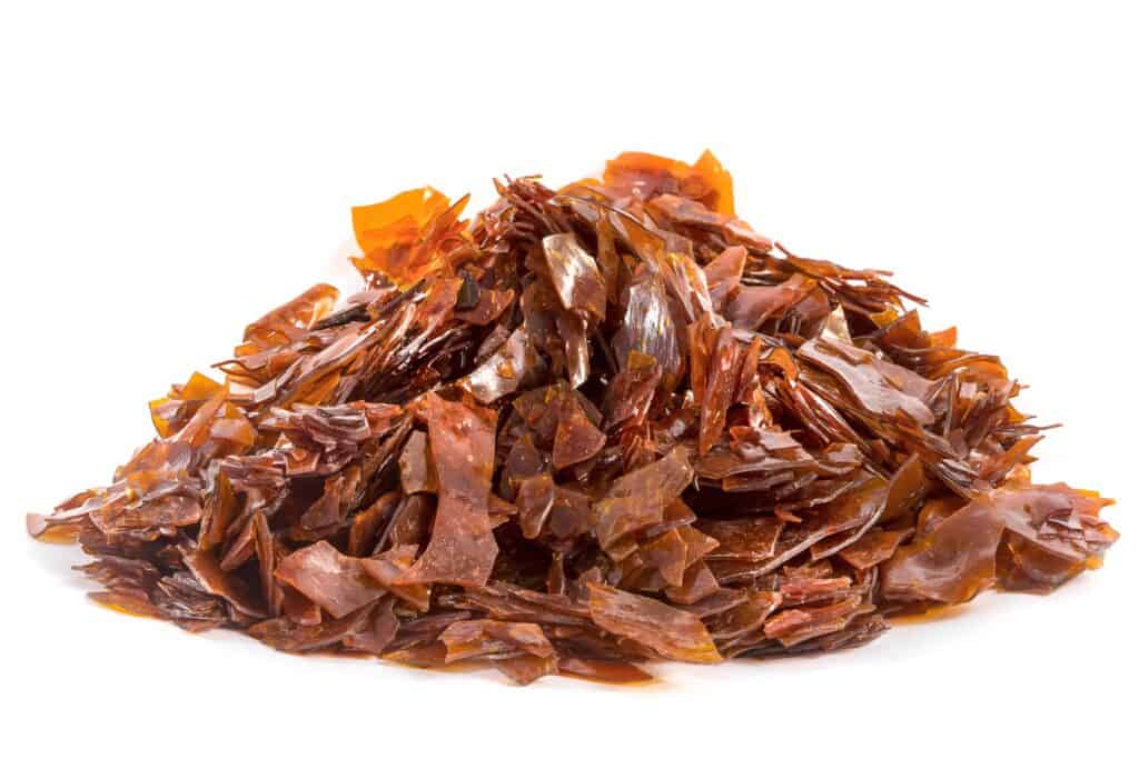 A pile of brown, translucent flakes of shellac on a white background.
