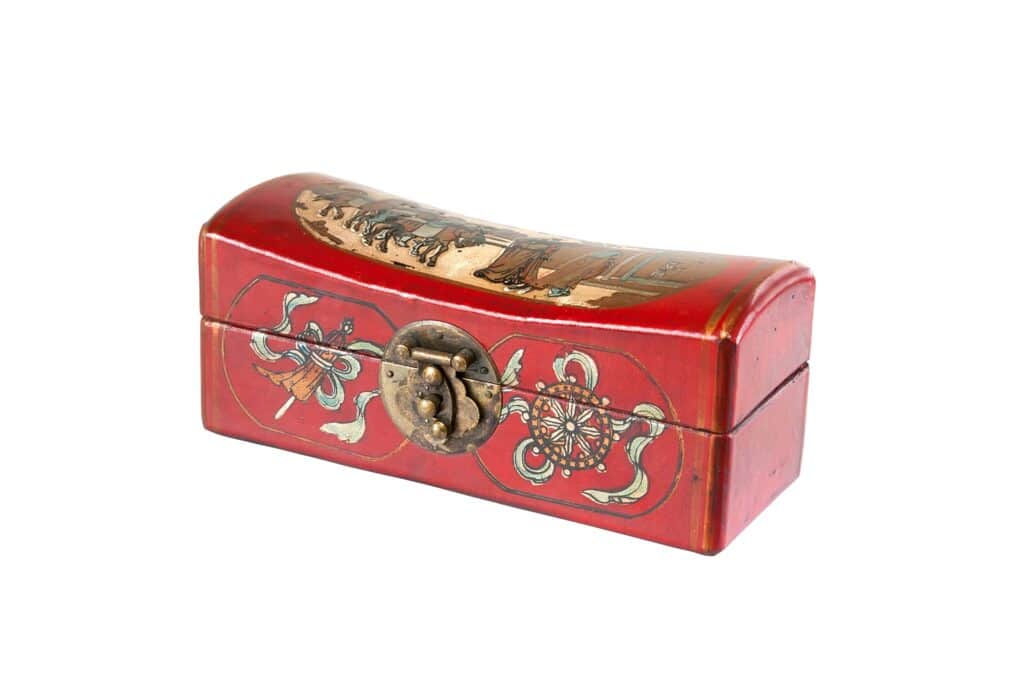 Rectangular red lacquered box with a curved lid, brass clasp, and painted decorative motifs including a floral pattern and a scene with figures.