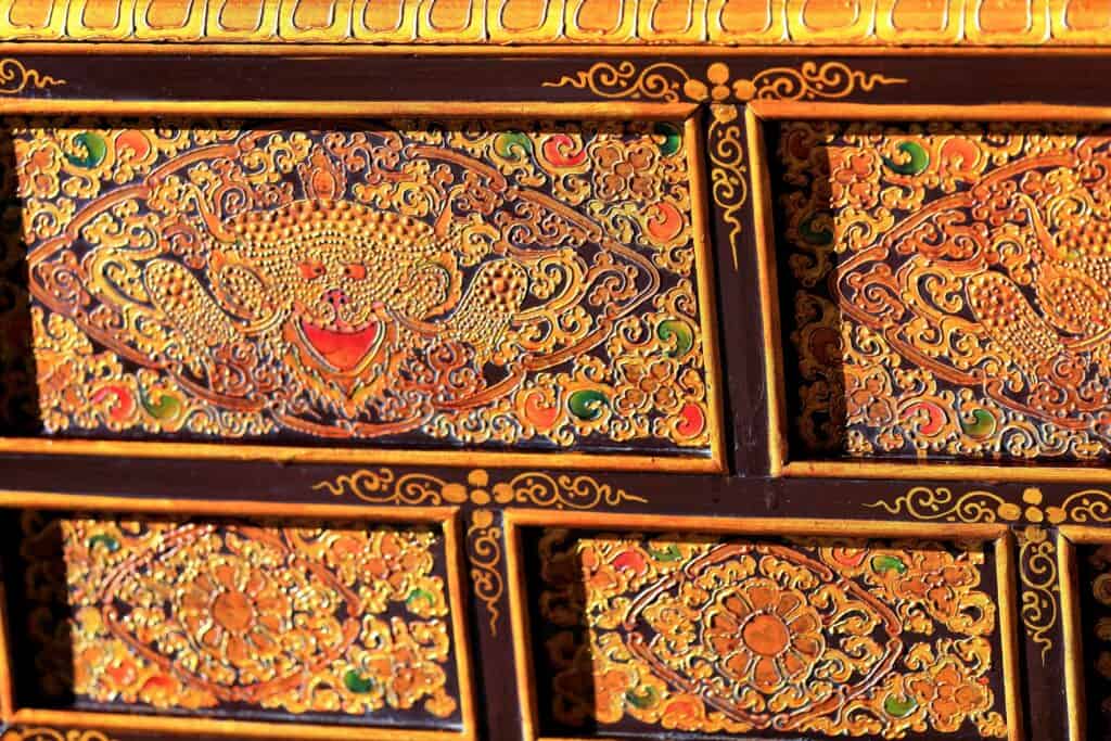 Ornate wooden panel featuring intricate gold, red, and green patterns with stylized carvings and decorative motifs.