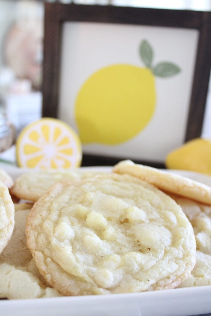 A plate of lemon cookies sits in front of framed lemon-themed artwork and lemon-shaped decorations.