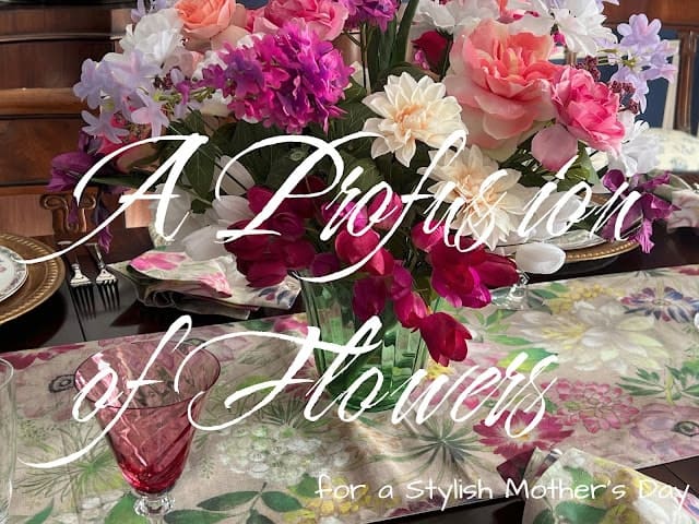 A table set for Mother's Day with a floral table runner, pink glassware, and a large bouquet of mixed flowers. Text reads: "A Profusion of Flowers for a Stylish Mother’s Day.
